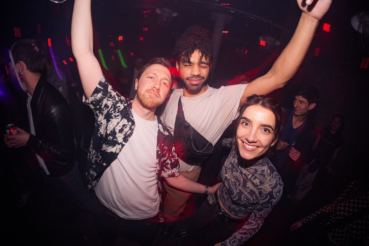 Drei lächelnde junge Erwachsene tanzen in einem schwach beleuchteten Club.